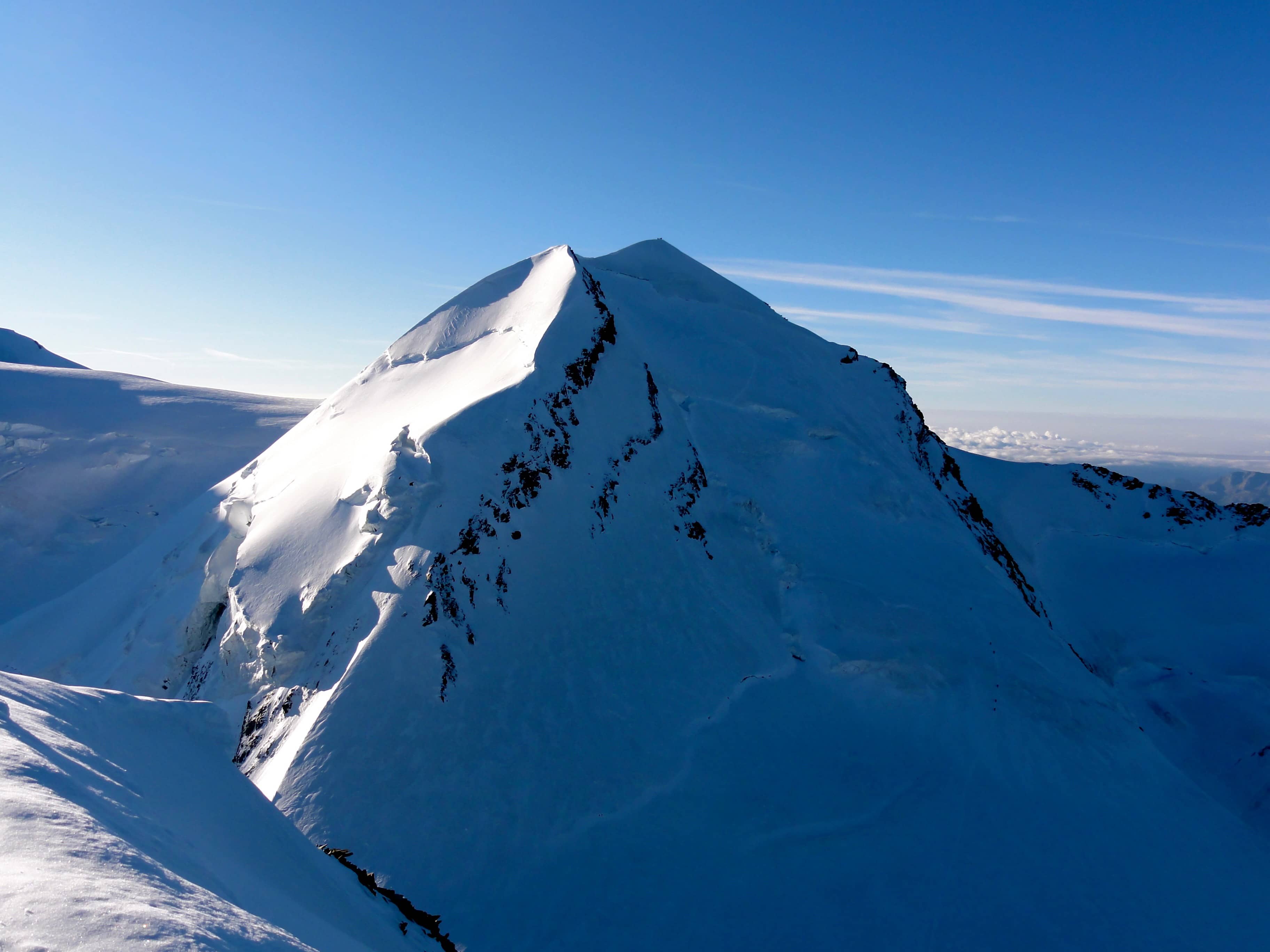 Der schneeweisse Castor vom Pollux aus gesehen. Der Aufstieg erfolgt über die schattige Westflanke (eine Seilschaft am Einstieg ist zu erkennen)